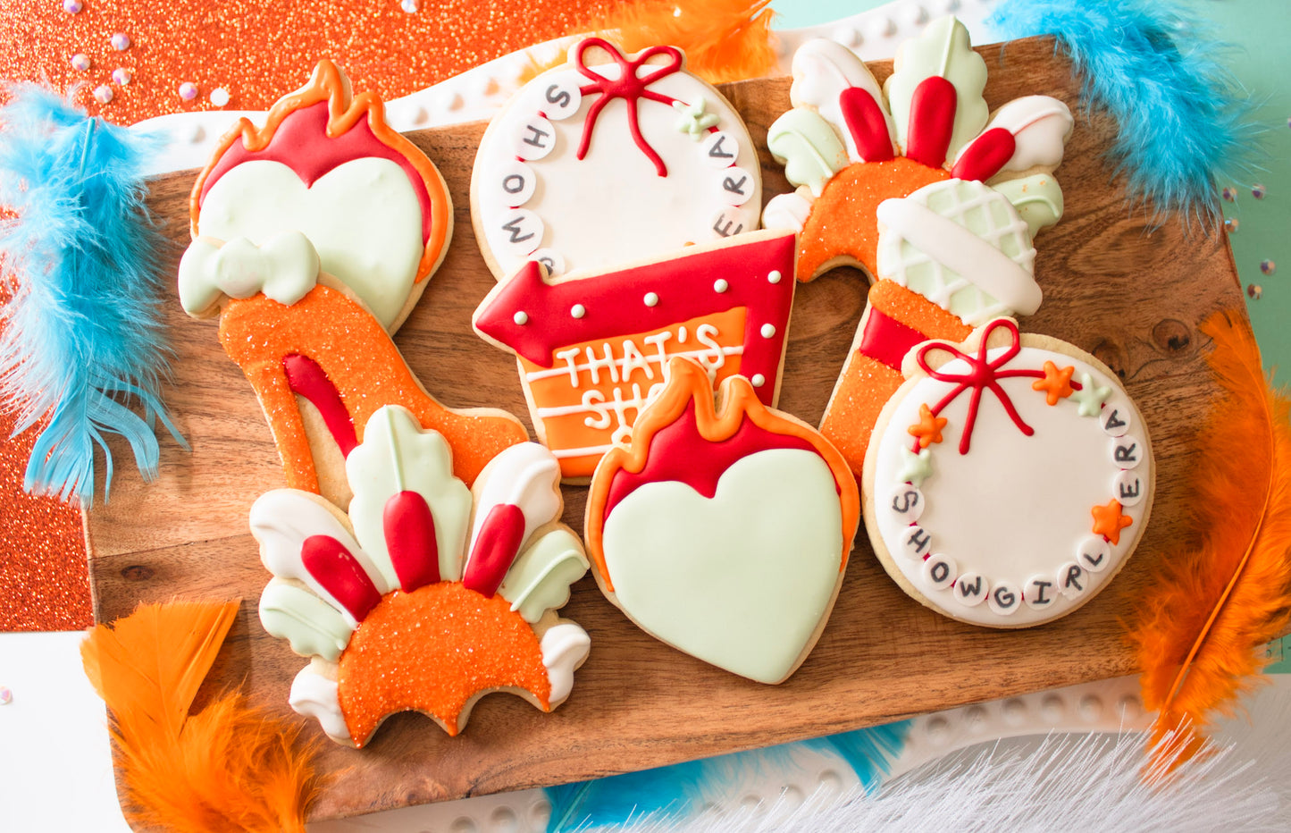 Decorative cookies shaped like a turkey, heart, and gift box on a wooden board with colorful feathers.