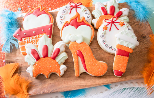 Decorative cookies shaped like high heels, ice cream cones, and other items on a wooden board.