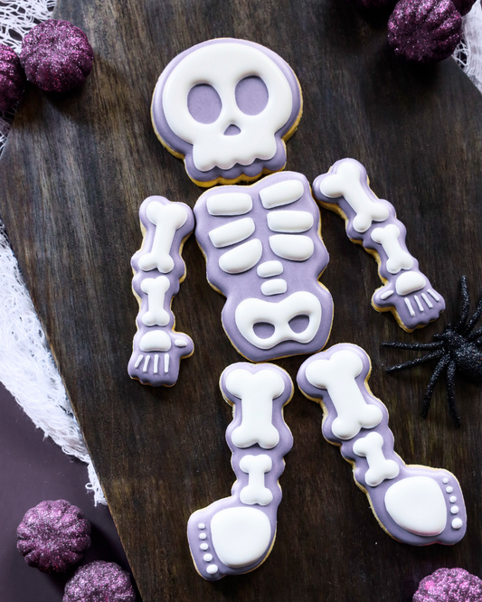 Skeleton cookie decoration on a wooden surface with purple decorative elements.